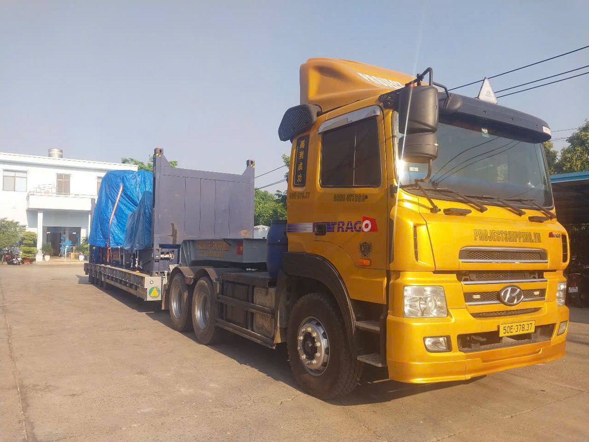 40ft flat rack with machinery under tarpaulin on a Project Shipping lowbed after customs clearance at Cat Lai