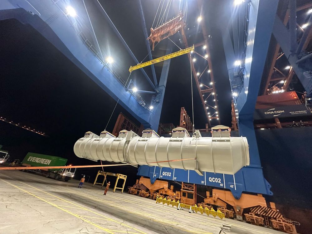 Breakbulk tank lifted by ship crane at night in a Vietnamese port