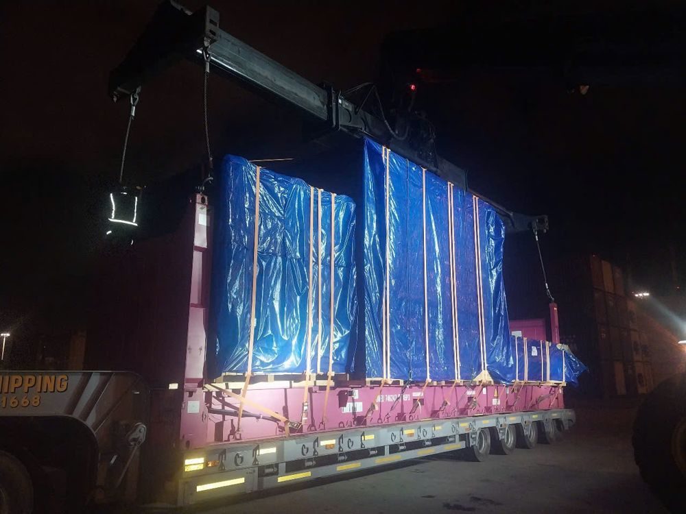 Crane lifting a wrapped machine onto a 40ft flat rack container at night at a Ho Chi Minh City port