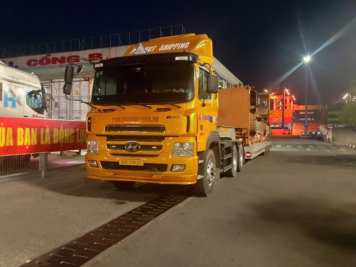 Excavators on a 40ft flat rack leaving Cat Lai port at night on a Project Shipping tractor