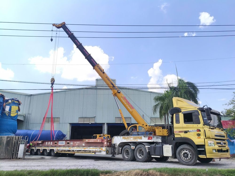 Mobile crane loading a cylindrical unit at a factory for export on flat rack containers via Cat Lai port