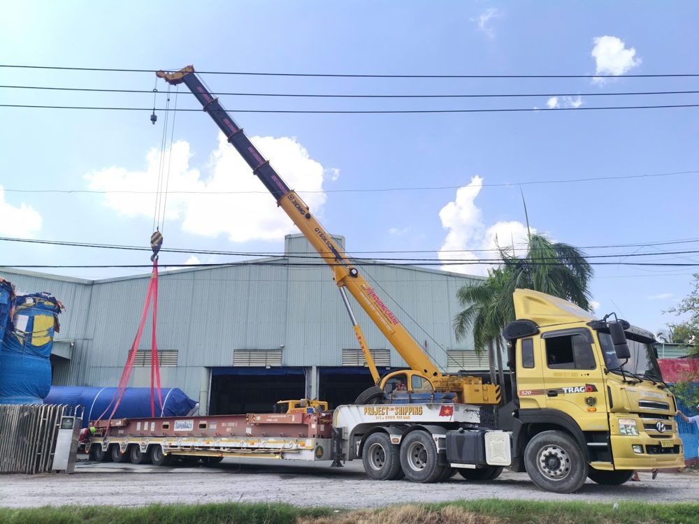 Mobile crane loading a cylindrical unit onto a Project Shipping lowbed at a factory