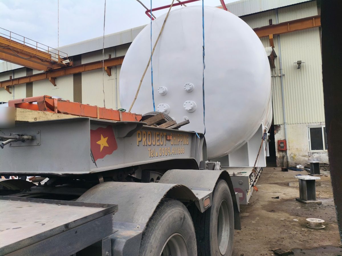 Project Shipping lowbed gooseneck with a white storage tank on deck before the run to Moc Bai